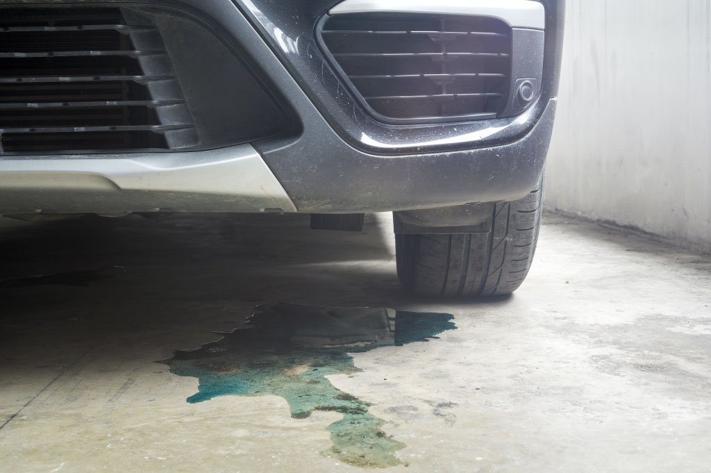 Green coolant puddle on the ground beneath the front bumper of a parked car