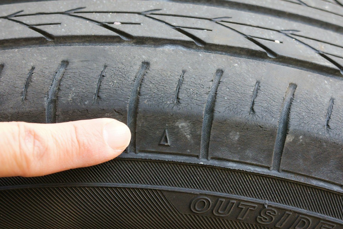 Finger pointing to the markings molded into the sidewall of a car tire