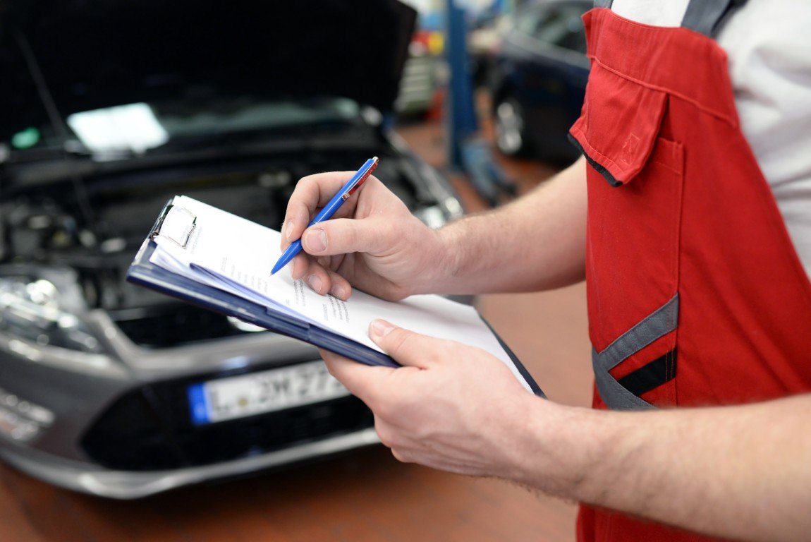 Technician documenting completed service work on a written record at a vehicle
