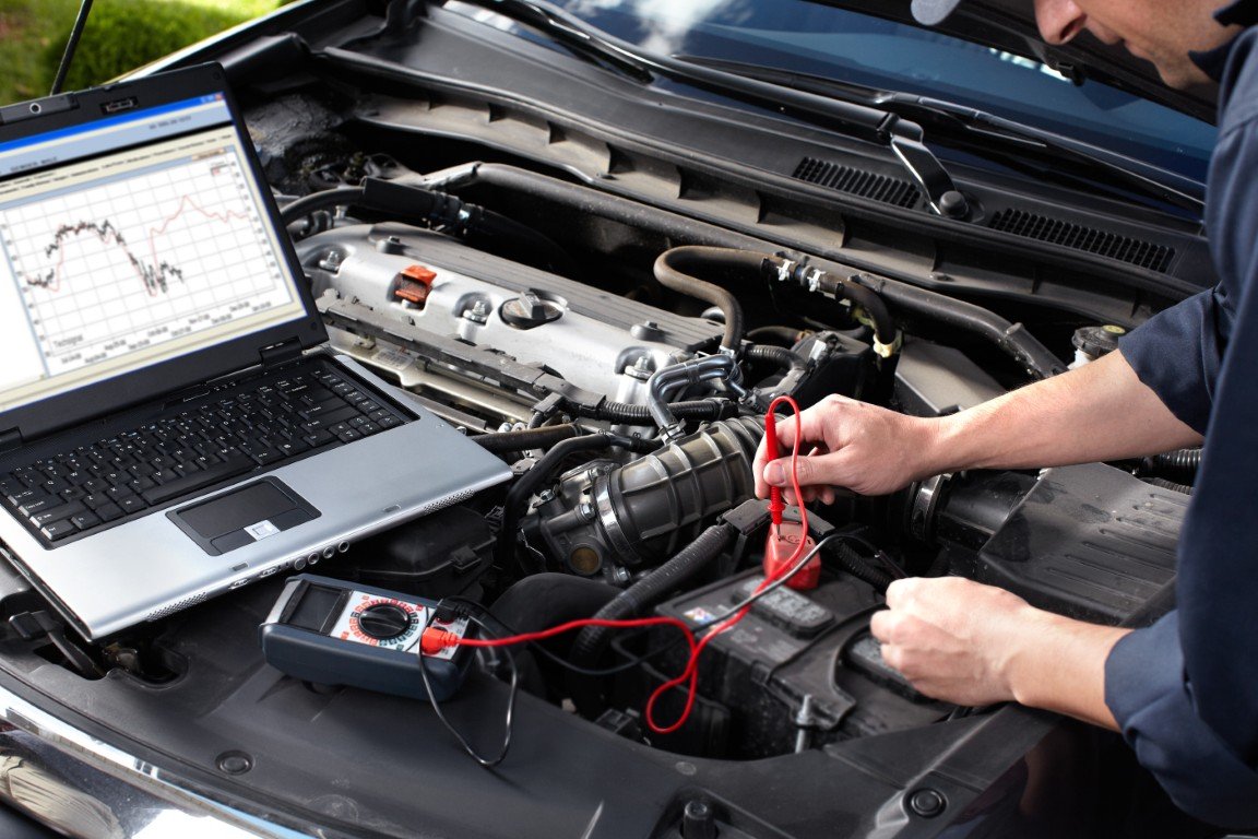 Technician using a multimeter and diagnostic laptop to test an engine