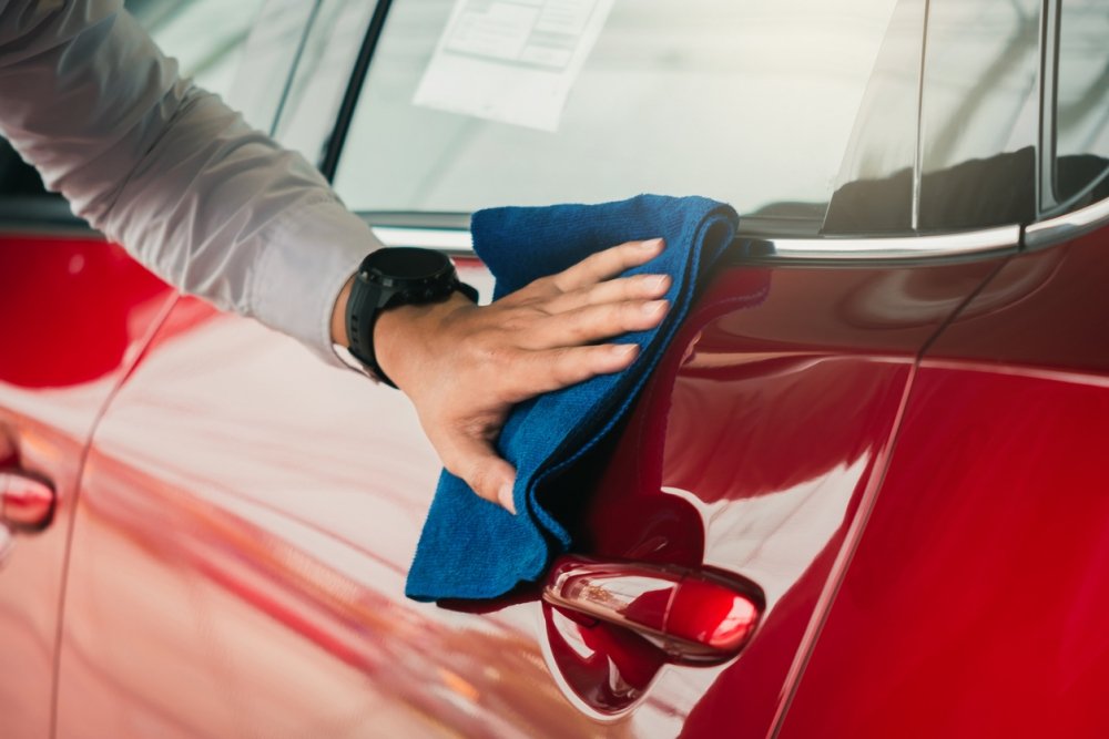 Hand polishing the paint of a red car with a microfiber cloth