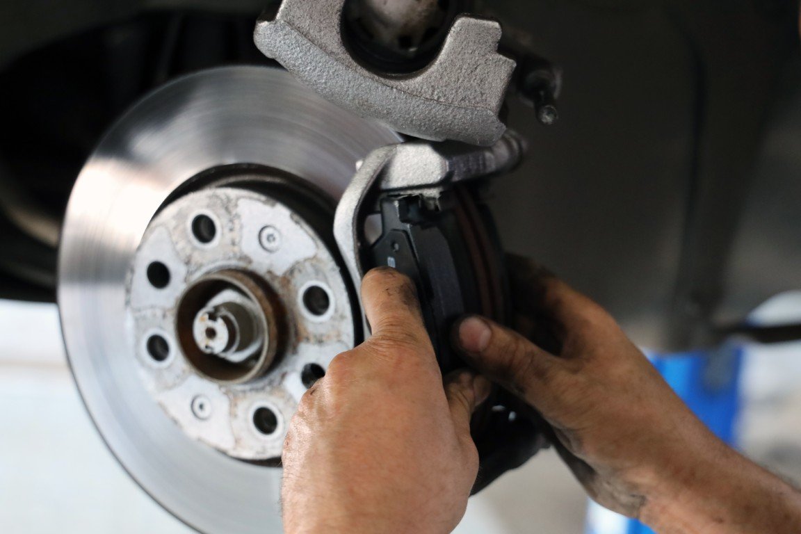 Technician servicing a brake caliper and rotor on a lifted vehicle